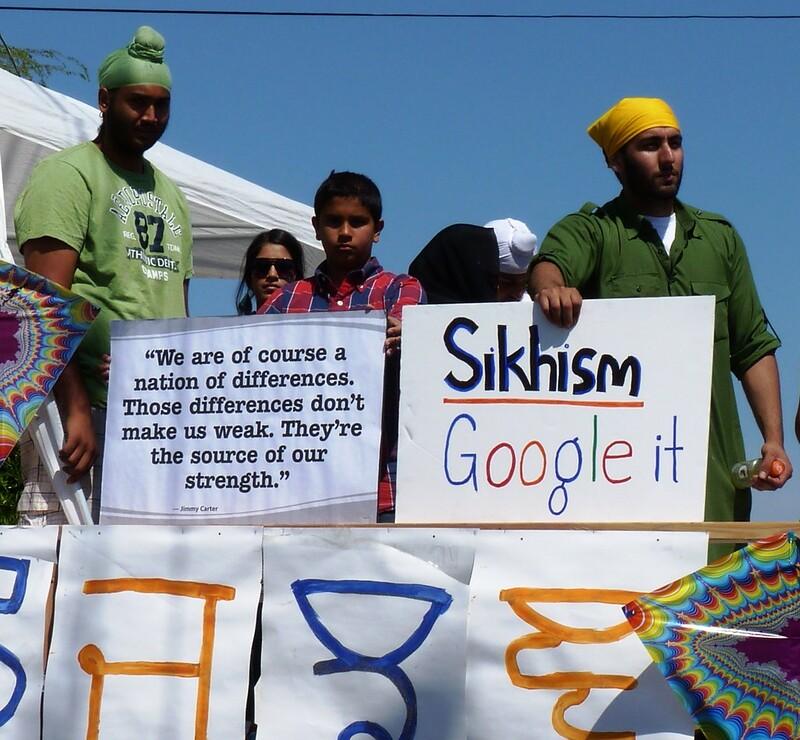 Photo of group of Sikhs at a community parade. One sign reads, "we are of course a nation of differences. Those differences don't make us weak. They're the source of our strength," which is a quote from Jimmy Carter.
